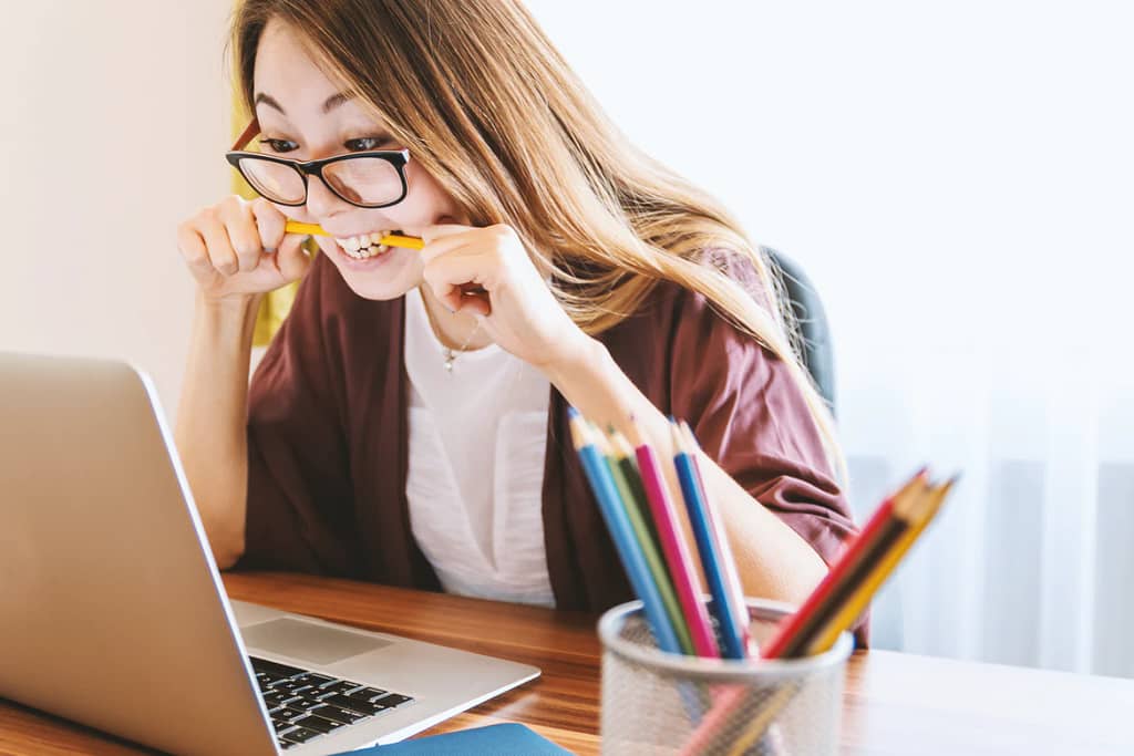 woman with glasses biting a pencil looking at her computer